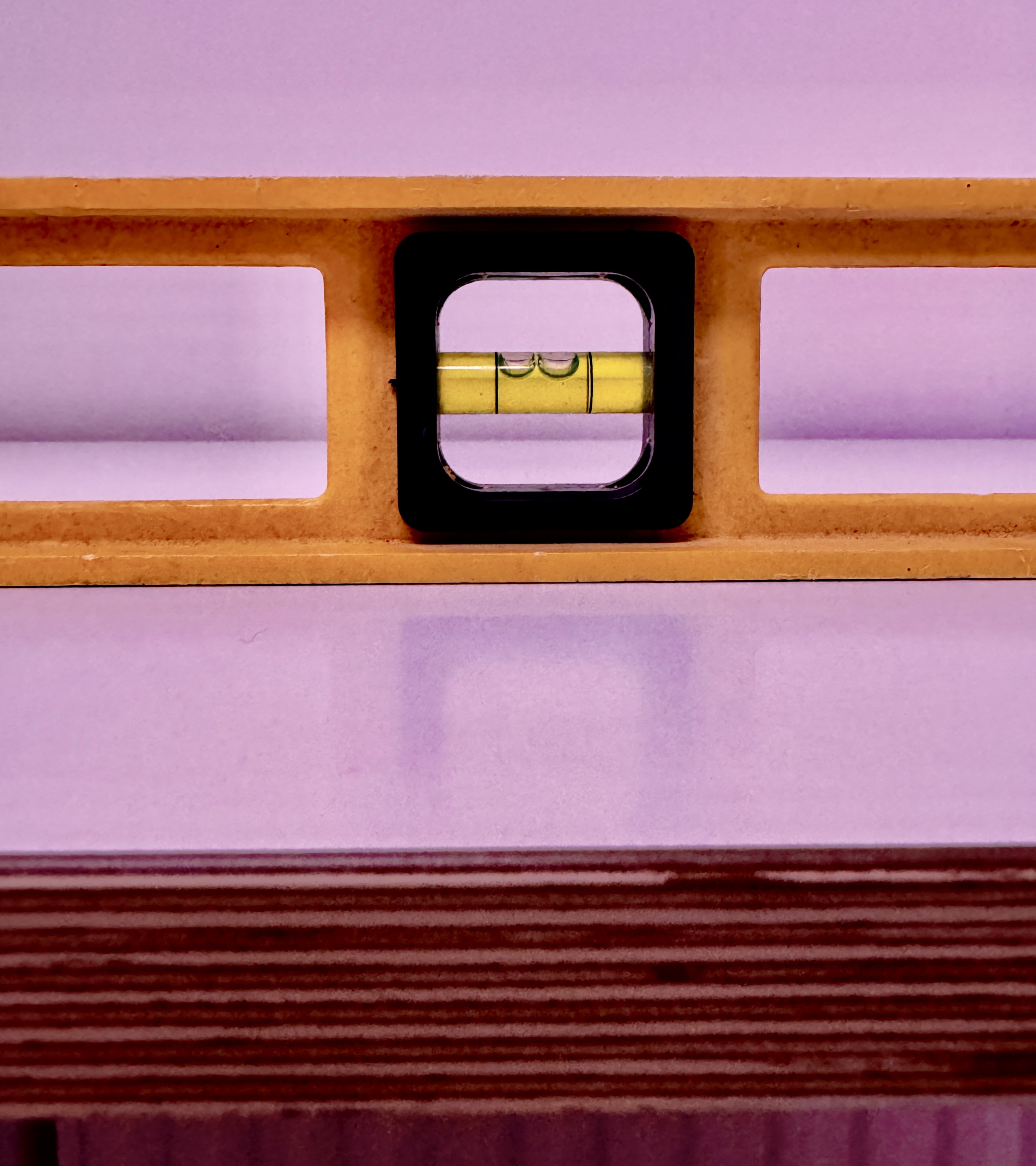 A yellow spirit level with 2 bubbles, with a plain pink background